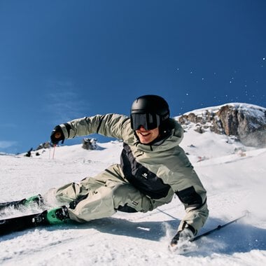 Skier in deep snow with a skier wearing a white ski suit, black helmet, under clear sky at Ski Alpin Ifen. | © Kleinwalsertal Tourismus eGen • Photographer: Oliver Farys
