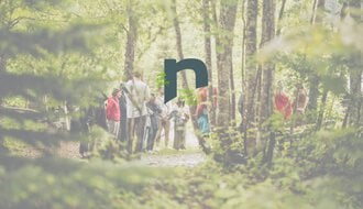 Group of people walking along a forest path in sunlight, with trees and green nature in the background.